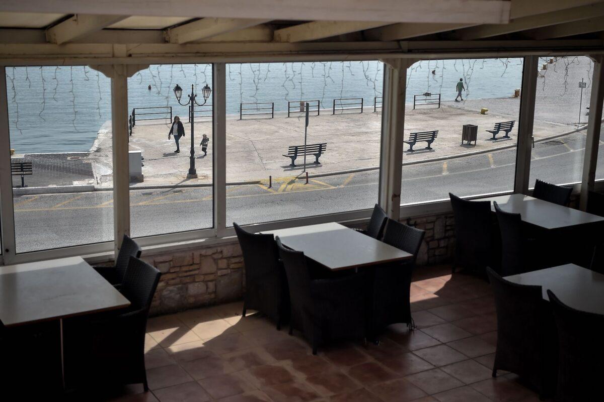 An empty restaurant, with people walking on a seafront promenade at the port town of Rafina near Athens, Greece, on April 29, 2020. (Louisa Gouliamaki/AFP/Getty Images)