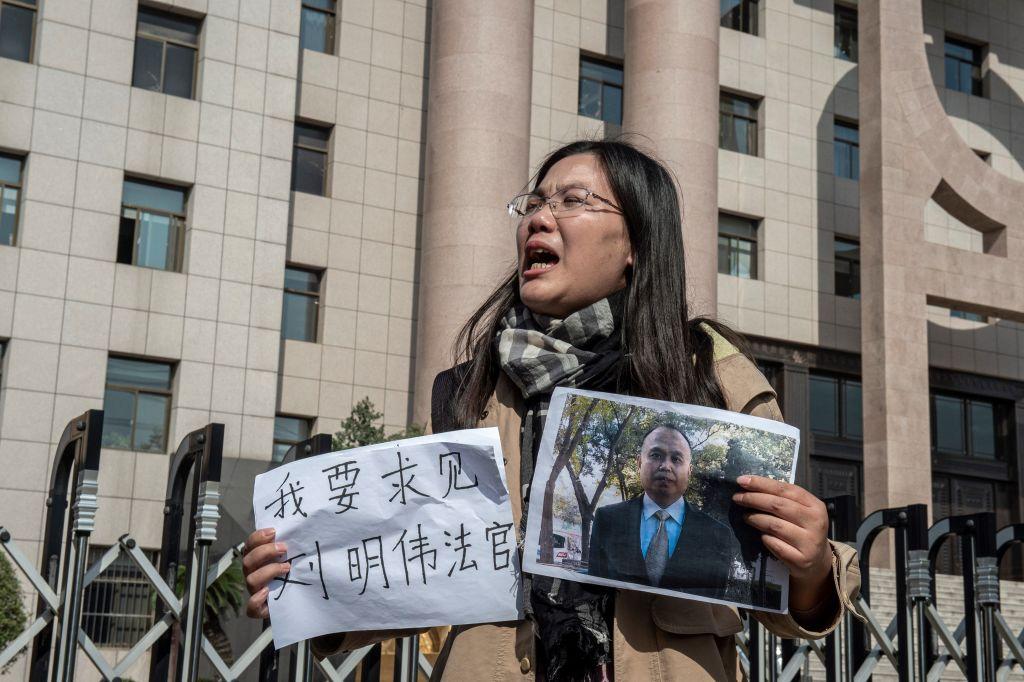 Xu Yan, wife of human rights lawyer Yu Wensheng, holds a piece of paper that reads, "I want to request a meeting with Judge Liu Mingwei" and a picture of her husband outside the Xuzhou Intermediate Peoples Court in Xuzhou, China, on Oct. 31, 2019. (Nicolas Asfouri/AFP via Getty Images)