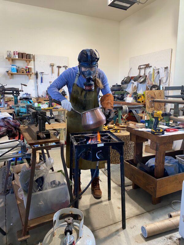 Sara Dahmen wears a gas mask and other protective gear while tinning her copper pieces. Here, Dahmen works on a vintage copper cooking pot in her shop. (Courtesy of Sara Dahmen)