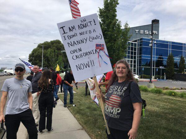 Tammy Mendoza (R) holds a sign during the rally in front of Tesla’s corporate office in Fremont, Calif., on May 13, 2020. (Ilene Eng/The Epoch Times)