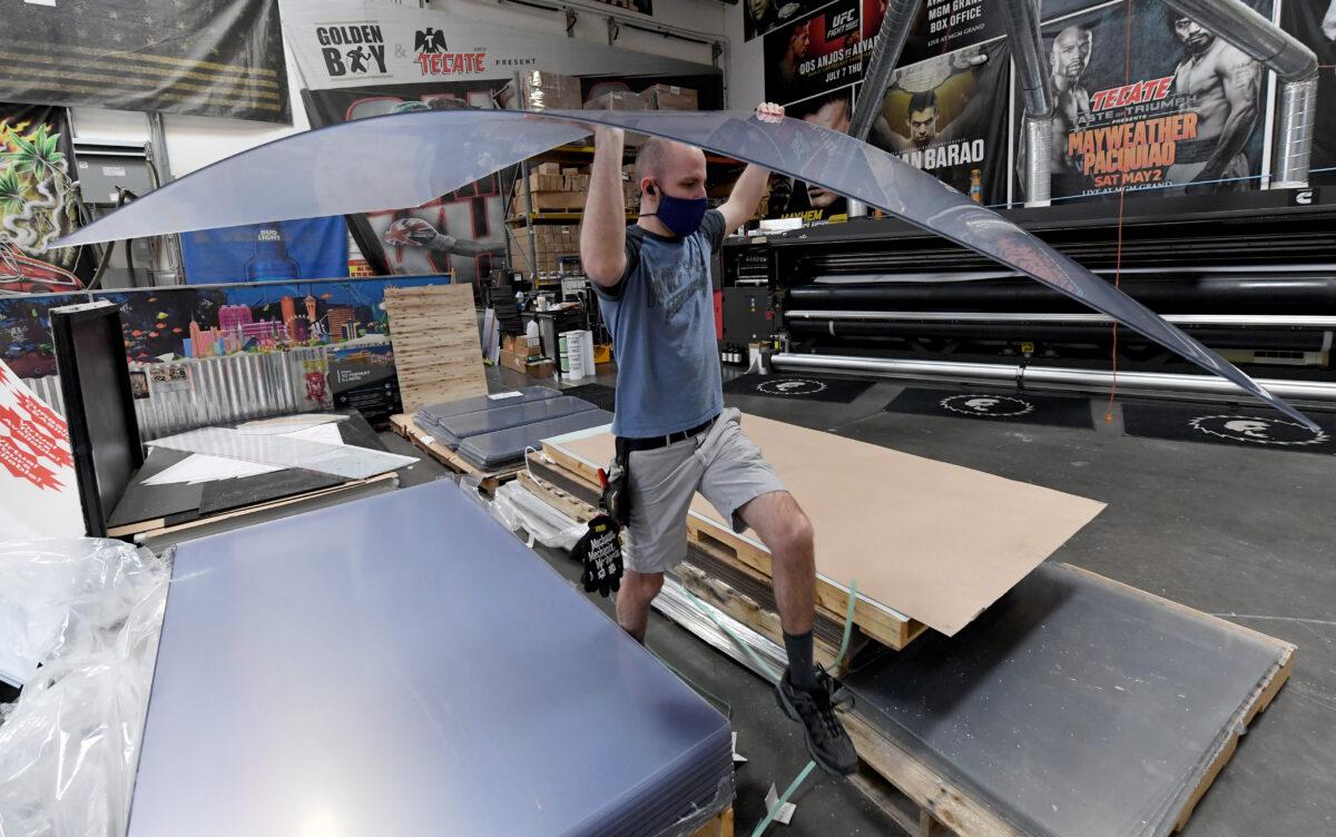 Jaeden Milam carries a sheet of acrylic to a computer-controlled cutting machine as he makes safety shield dividers at Screaming Images amid the spread of the coronavirus in Las Vegas, Nev. on May 18, 2020. (Ethan Miller/Getty Images)