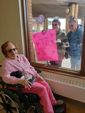 Gladys McDade celebrates her 90th birthday at a nursing home in Melville, Saskatchewan, while her family members visit with her through the window. (Courtesy Valerie Exner)