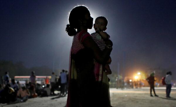 A woman and her baby wait for a bus to take them to a railway station to board a train to their home state of Uttar Pradesh, after a limited reopening of India's giant rail network following a nearly seven-week lockdown to slow the spreading of the CCP virus, in Ghaziabad in the outskirts of New Delhi, India, on May 18, 2020. (Adnan Abidi/Reuters)
