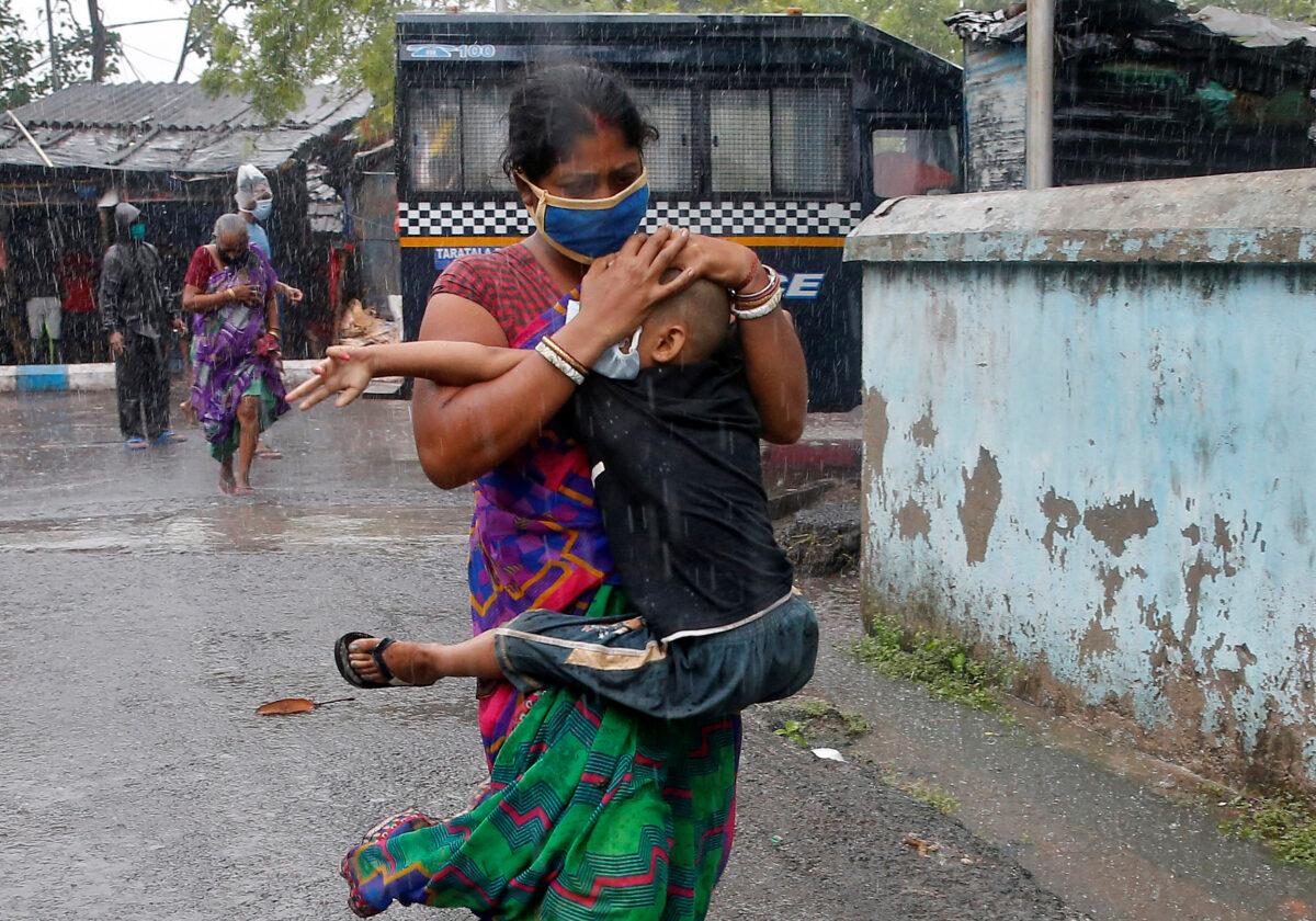 A woman carries her son as she tries to protect him from heavy rain while they rush to a safer place, following their evacuation from a slum area before Cyclone Amphan makes its landfall, in Kolkata, India, on May 20, 2020. (Rupak De Chowdhuri/Reuters)