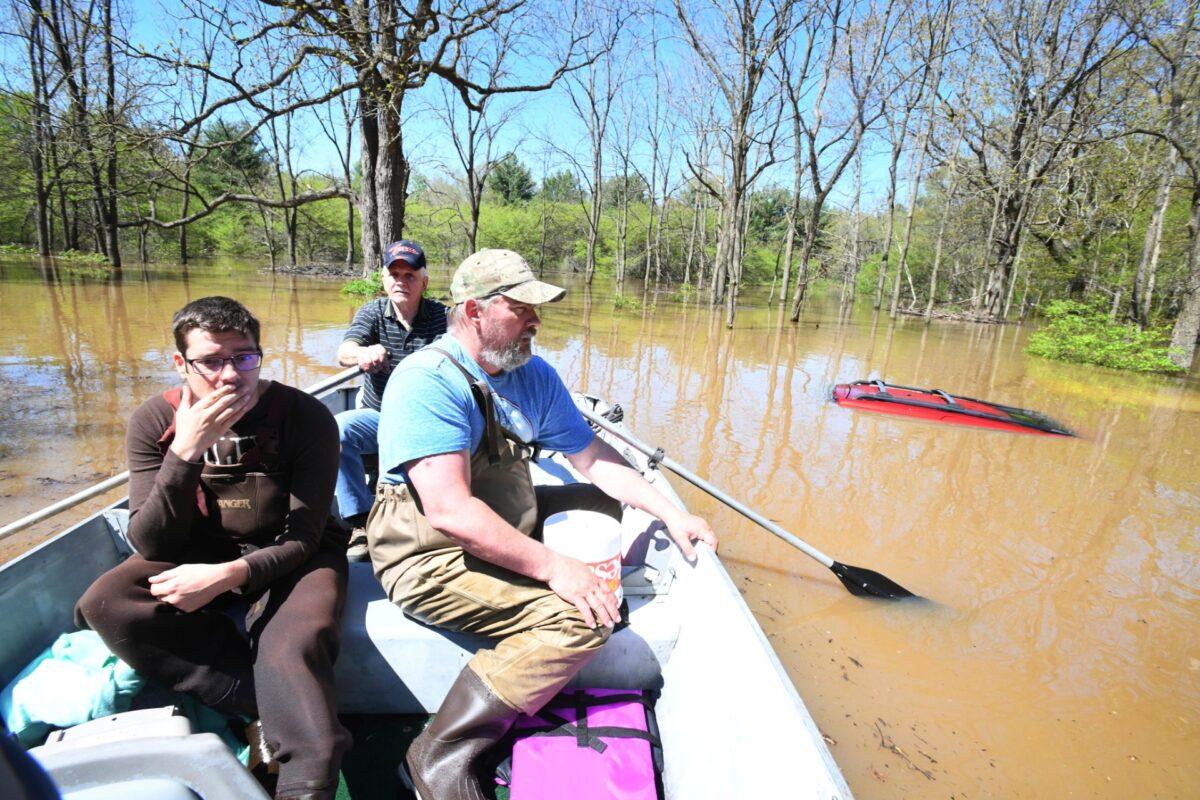 Don Thomas rows Nick Maki (L) and son Jason Thomas past Jason's red 2001 Jeep Grand Cherokee, barely visible above the flooding, after picking up Jason's two family cats from his flooded home in Midland. Breached dams further up the Tittabawassee River flooded downtown Midland, Mich., on May 20, 2020. (Daniel Mears/ The Detroit News via AP)