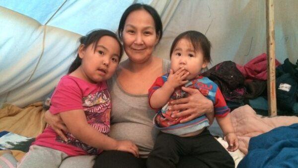 Alison Nakoolak with two of her children in a tent in Iqaluit in November 2015. Nakoolak, her husband, and their four children lived in this tent for three months over the winter. At least 5,000 Inuit need housing, and some prefer to live in a tent rather with relatives in already overly crowded homes. (John Van Dusen/CBC)