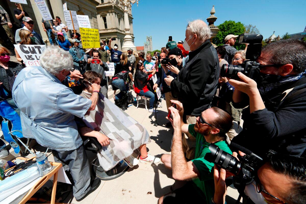 The media record barber Karl Manke, of Owosso, giving a free haircut to Parker Shonts on the steps of the State Capitol during a rally in Lansing, Mich., on May 20, 2020. (Paul Sancya/AP Photo)