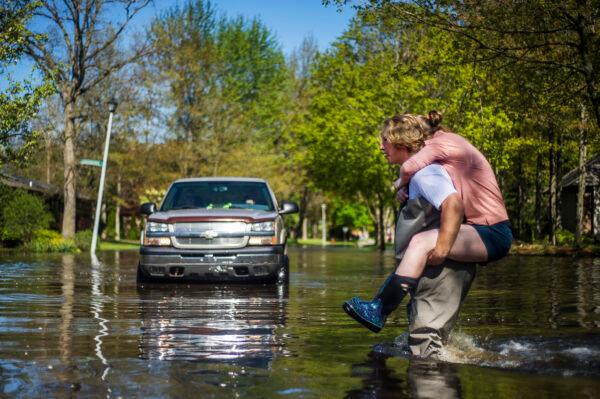 Ryan Stadelmaier, 16, gives a piggyback ride to his sister Rachel Stadelmaier, 27, as they cross Walden Woods Drive while helping residents tend to their flooded homes, in Midland, Mich., on May 20, 2020. (Katy Kildee/Midland Daily News via AP)