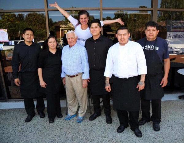 Katia Bagatta stretches her arms while standing behind her father and employees at Bistro K restaurant in Laguna Niguel, Calif. (Courtesy of Katia Bagatta)