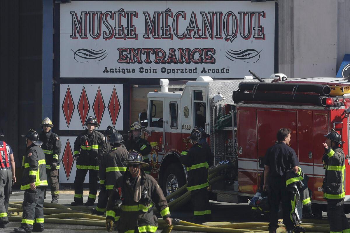 Fire officials work in front of a sign for Musee Mecanique after a fire broke out before dawn at Fisherman's Wharf in San Francisco, Saturday, May 23, 2020. (AP Photo/Jeff Chiu)