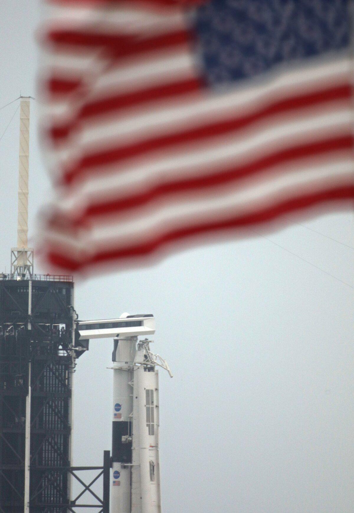 An American flag flutters above the crew access arm (top C) which is seen leading to the Crew Dragon spacecraft atop a SpaceX Falcon 9 rocket, at launch complex 39A at the Kennedy Space Center in Florida on May 25, 2020. (Gregg Newton/AFP via Getty Images)