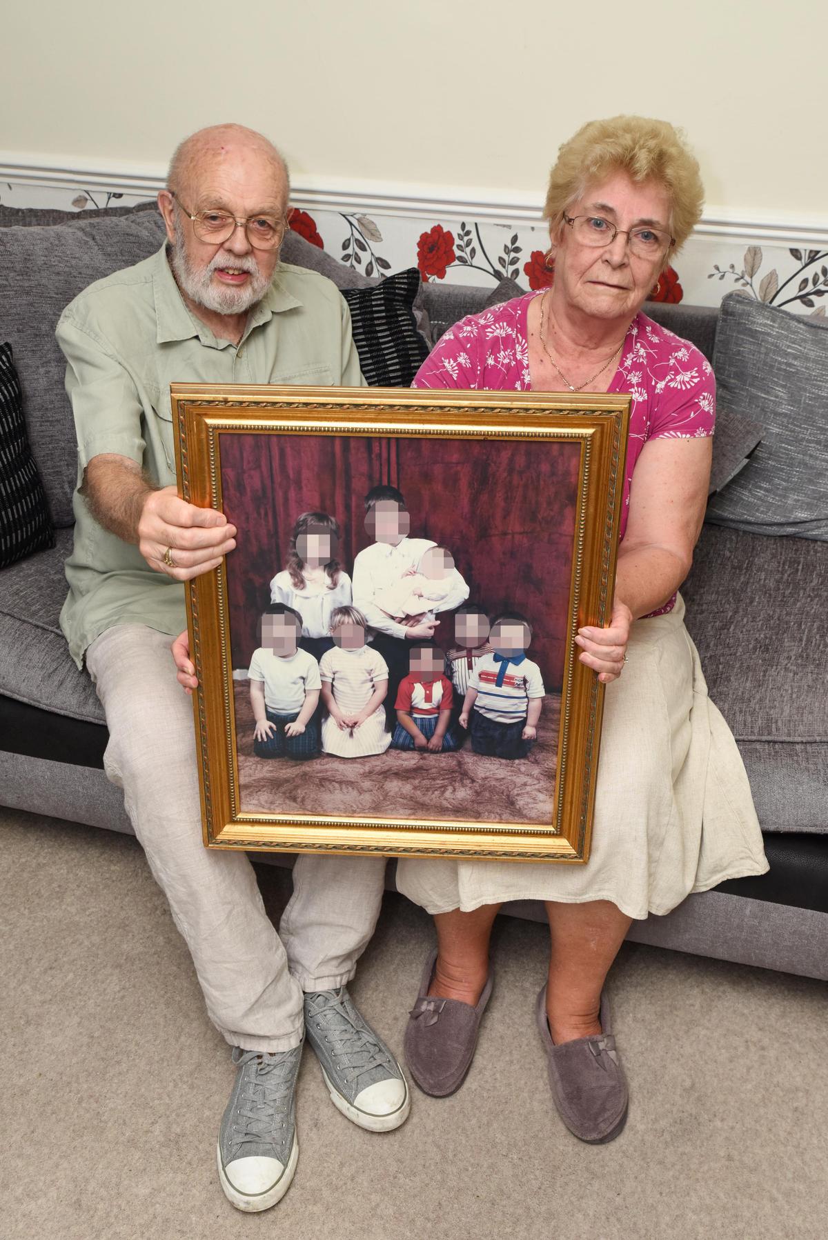 William Foster and his wife, Jean, holding a pixelated image of some of their fostered children on June 17, 2019. (Caters News)