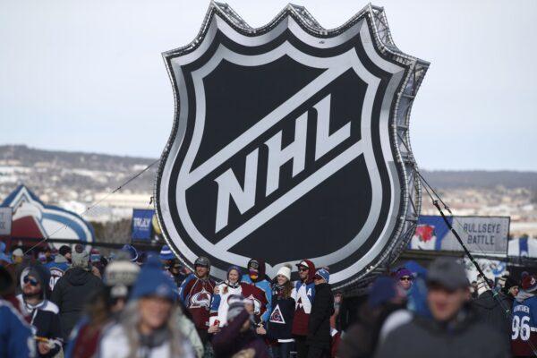 Fans pose below the NHL league logo at a display outside Falcon Stadium before an NHL Stadium Series outdoor hockey game between the Los Angeles Kings and Colorado Avalanche, at Air Force Academy, Colo., on Feb. 15, 2020. (David Zalubowski/AP Photo)