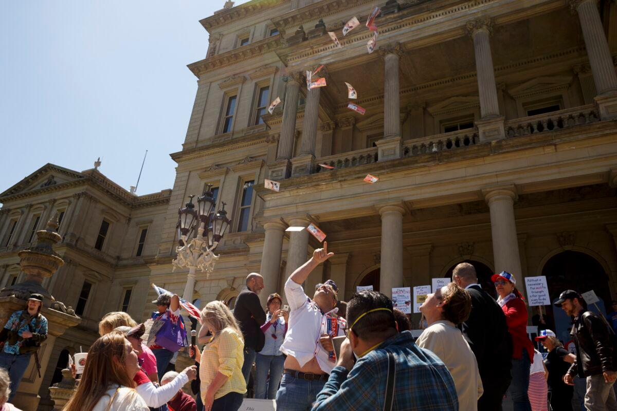  A protester throws fake money with President Trump's face on it into the air on the steps of the state Capitol during Operation Haircut in Lansing, Michigan, on May 20, 2020. The protest was part of a national movement against stay-at-home orders. (Elaine Cromie/Getty Images)