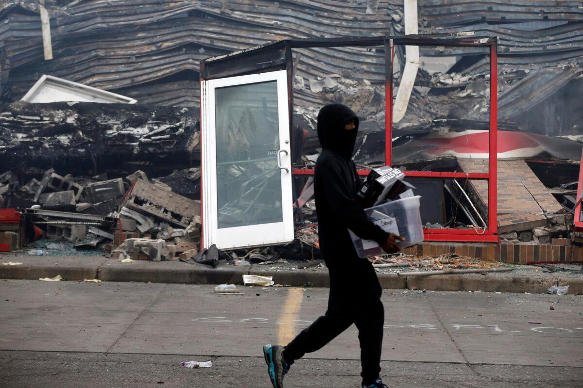A man carries items past a burned out Auto Zone store after a night of rioting and looting near the Minneapolis Police Third Precinct in Minneapolis, Minn., on May 28, 2020, (Jim Mone/AP photo)