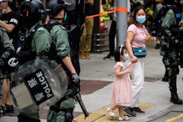 A woman and a young child walk past riot police standing guard on a street in the Mongkok district of Hong Kong on May 27, 2020. (Anthony Wallace/AFP via Getty Images)