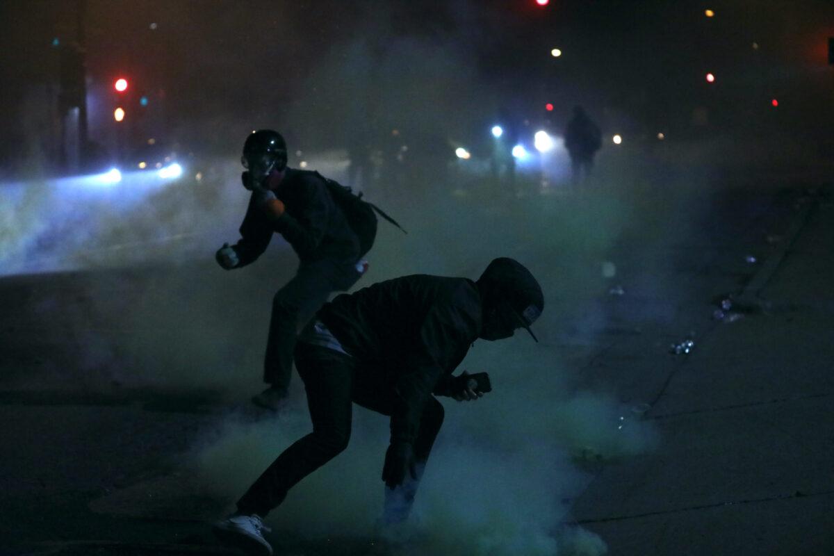 A rioter tries to grab a tear gas canister and lob it back toward the police outside the Minneapolis Police 5th Precinct during the fourth night of protests and violence following the death of George Floyd, in Minneapolis, Minn., on May 29, 2020. (Charlotte Cuthbertson/The Epoch Times)