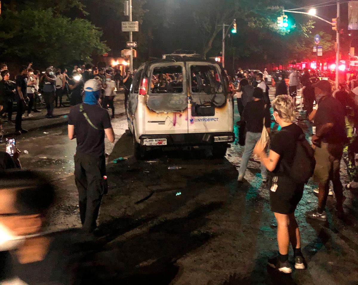 Protesters stand near a burned New York City Police Department van in the Brooklyn borough of New York on May 29, 2020. (Jim Mustian/AP Photo)
