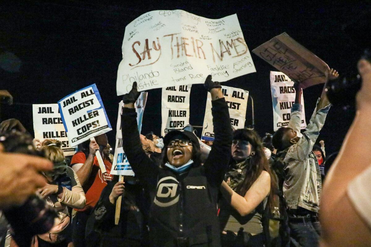 Protesters hold signs outside the Minneapolis Police 5th Precinct during the fourth night of protests and violence following the death of George Floyd, in Minneapolis, Minn., on May 29, 2020. (Charlotte Cuthbertson/The Epoch Times)