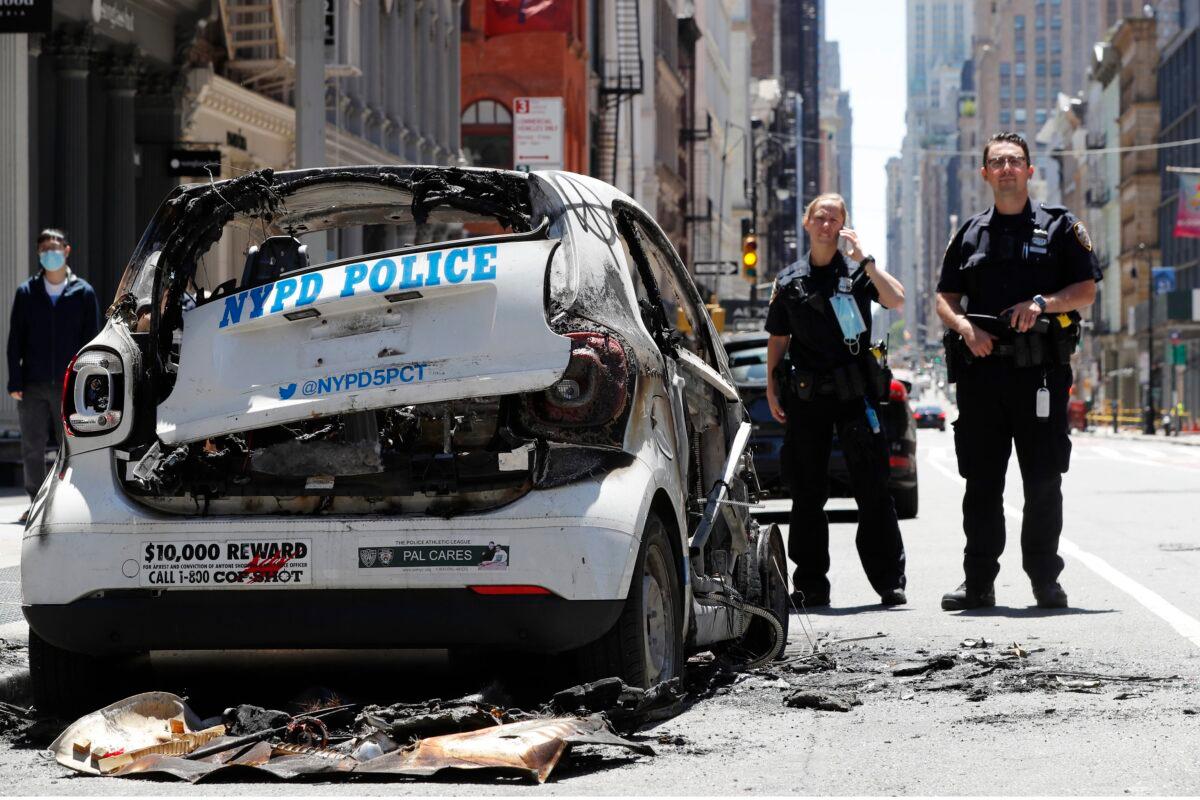 Officers stand guard beside a burned-out mini New York Police Department vehicle, abandoned on Broadway in Lower Manhattan on May 31, 2020. (Kathy Willens/AP Photo)