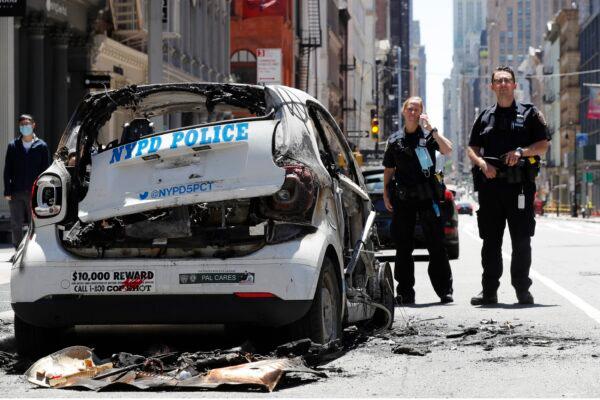 Officers stand guard beside a burned-out mini-New York Police Department vehicle, abandoned on Broadway in Lower Manhattan in New York, N.Y. on May 31, 2020. (Kathy Willens/AP Photo)