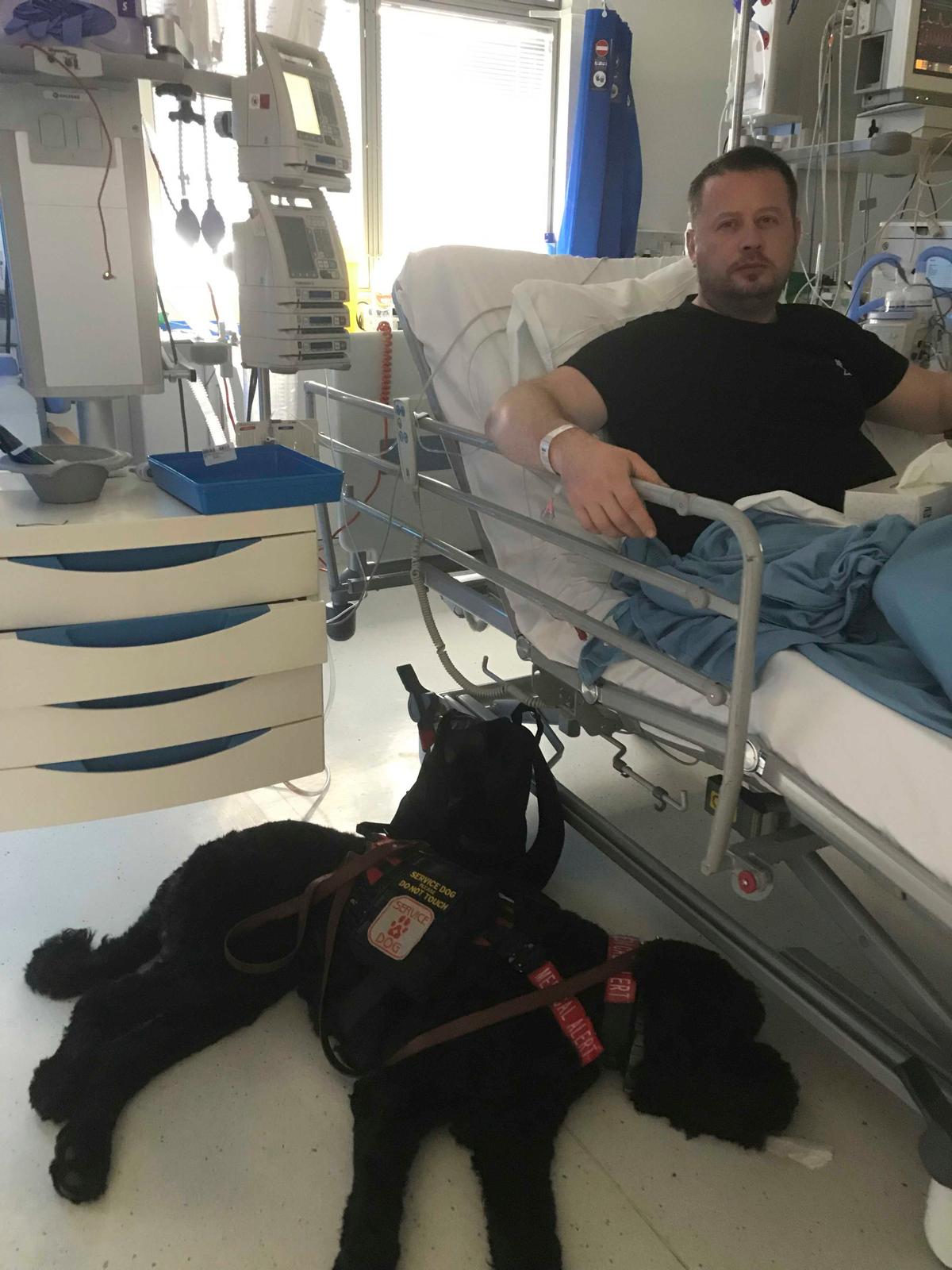 Jonathon Sheldon, 45, with service dog Teddy, in hospital (Caters News)