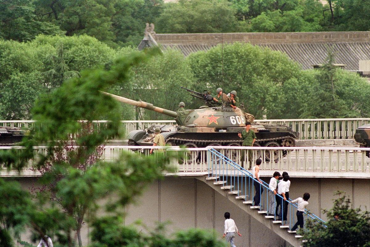 Chinese onlookers run away as a soldier threatens them with a gun while tanks took position at Beijing's key intersections next to the diplomatic compound on June 5, 1989. (Catherine Henriette/AFP via Getty Images)