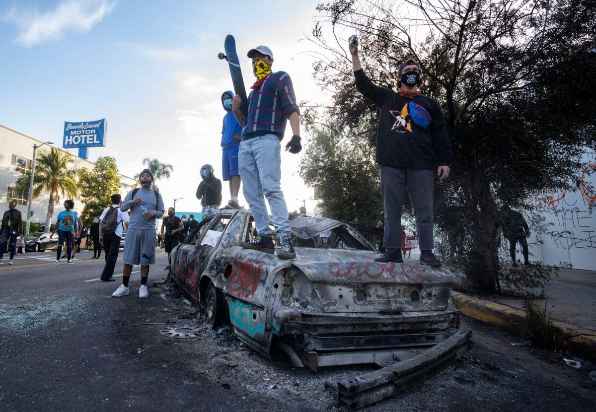 Protesters stand on top of a burned vehicle during a demonstration over the death of George Floyd in Los Angeles, Calif. on May 30, 2020. (Christian Monterrosa/AP Photo)