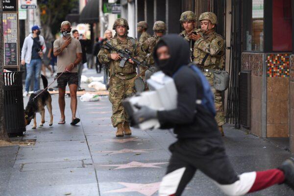 A suspected looter carrying boxes of shoes runs past National Guard soldiers in Hollywood, California, on June 1, 2020. (Robyn Beck/AFP via Getty Images)