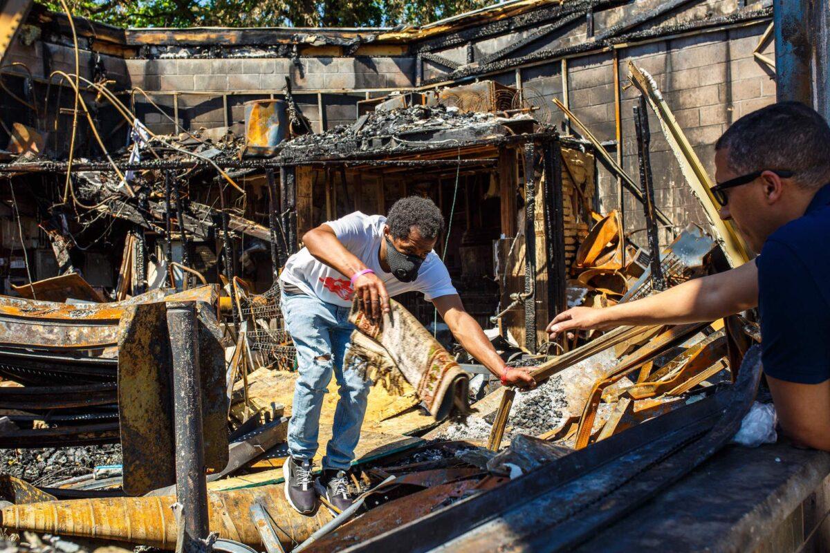 An employee hands an item to a gas station owner from the charred wreckage of the business destroyed during last week's rioting, in Minneapolis, Minn., on June 3, 2020. (Kerem Yucel/AFP/Getty Images)
