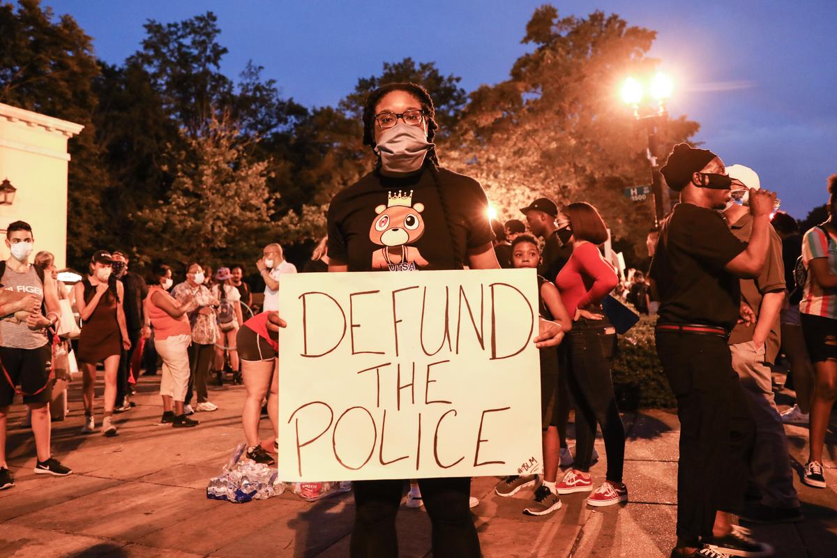 A protester holds a “Defund the Police” sign during a protest near the White House following the May 25 death of George Floyd in police custody, in Washington on June 6, 2020. (Charlotte Cuthbertson/The Epoch Times)