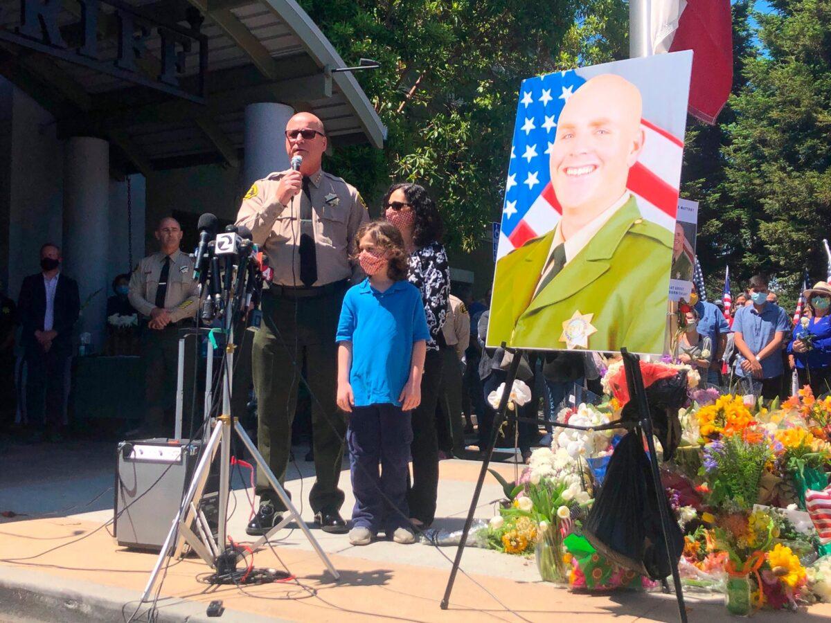 Santa Cruz Sheriff Jim Hart stands next to Hart's wife and child and a photo of fallen Sgt. Damon Gutzwiller, as more than a thousand people gather outside the Santa Cruz County Sheriff-Coroner's Office to pay their respects in Santa Cruz, Calif., on June 7, 2020. (Martha Mendoza/AP Photo)