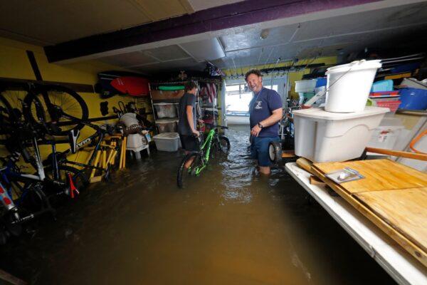 Rudy Horvath Jr., (L) moves his bicycle from his home, a boathouse in the West End section of New Orleans, as his father, Rudy Horvath Sr. (R) looks on after it took on water from a rising storm surge from Lake Pontchartrain in advance of Tropical Storm Cristobal, New Orleans, La., on June 7, 2020. (Gerald Herbert/AP Photo)