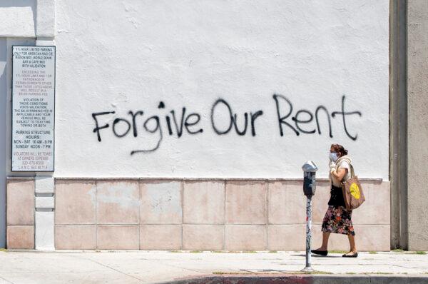 A woman wearing a mask walks past a wall bearing graffiti that asks for rent forgiveness amid the COVID-19 pandemic, in Los Angeles, Calif., on May 1, 2020. (Valerie Macon/AFP/Getty Images)