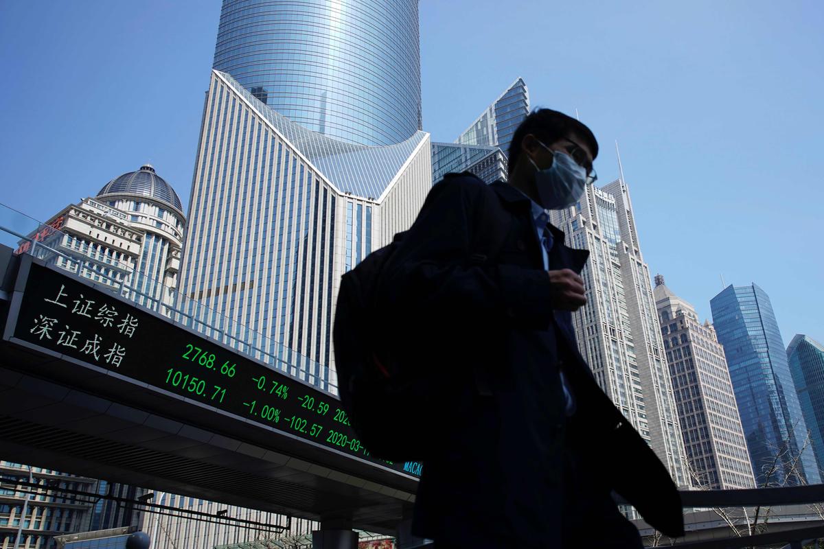 A pedestrian wearing a face mask walks near an overpass with an electronic board showing stock information, following an outbreak of the coronavirus disease (COVID-19), at Lujiazui financial district in Shanghai, China, on March 17, 2020. (Aly Song/Reuters)