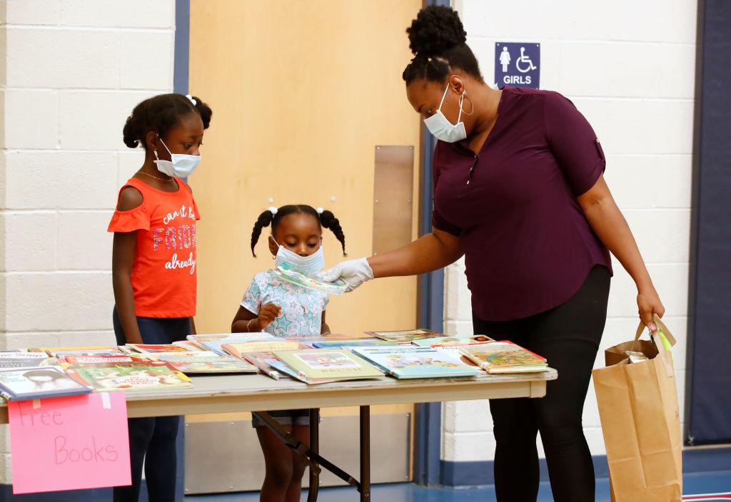 A parent and her children look over the free book table after picking up their personal belongings that have been put in a paper bag in the gym at Freedom Preparatory Academy in Provo, Utah, on May 18, 2020. (George Frey/Getty Images)