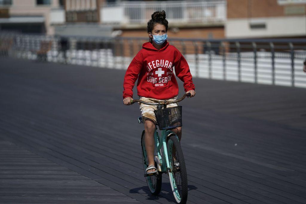 A young girl in a mask rides her bike along the boardwalk in Long Beach, New York May 22, 2020, as people get started on the Memorial Day weekend. (Timothy A. Clary/AFP via Getty Images)