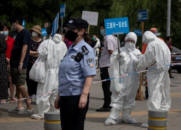 Medical staff in full protective gear carry signs to assist people who live near or who have visited the Xinfadi Market, a wholesale food market where a new CCP virus cluster has emerged, as they arrive for testing in Beijing, China, on June 17, 2020. (Noel Celis/AFP/Getty Images)