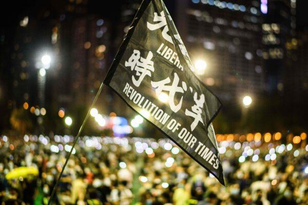 Attendees raise a flag that reads 'Liberate Hong Kong, Revolution Of Our Times' during a candlelit remembrance in Victoria Park in Hong Kong on June 4, 2020. (ANTHONY WALLACE/AFP via Getty Images)
