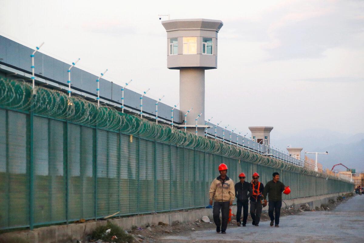 Workers walk by the perimeter fence of an internment camp in Xinjiang on Sept. 4, 2018. (Thomas Peter/Reuters)