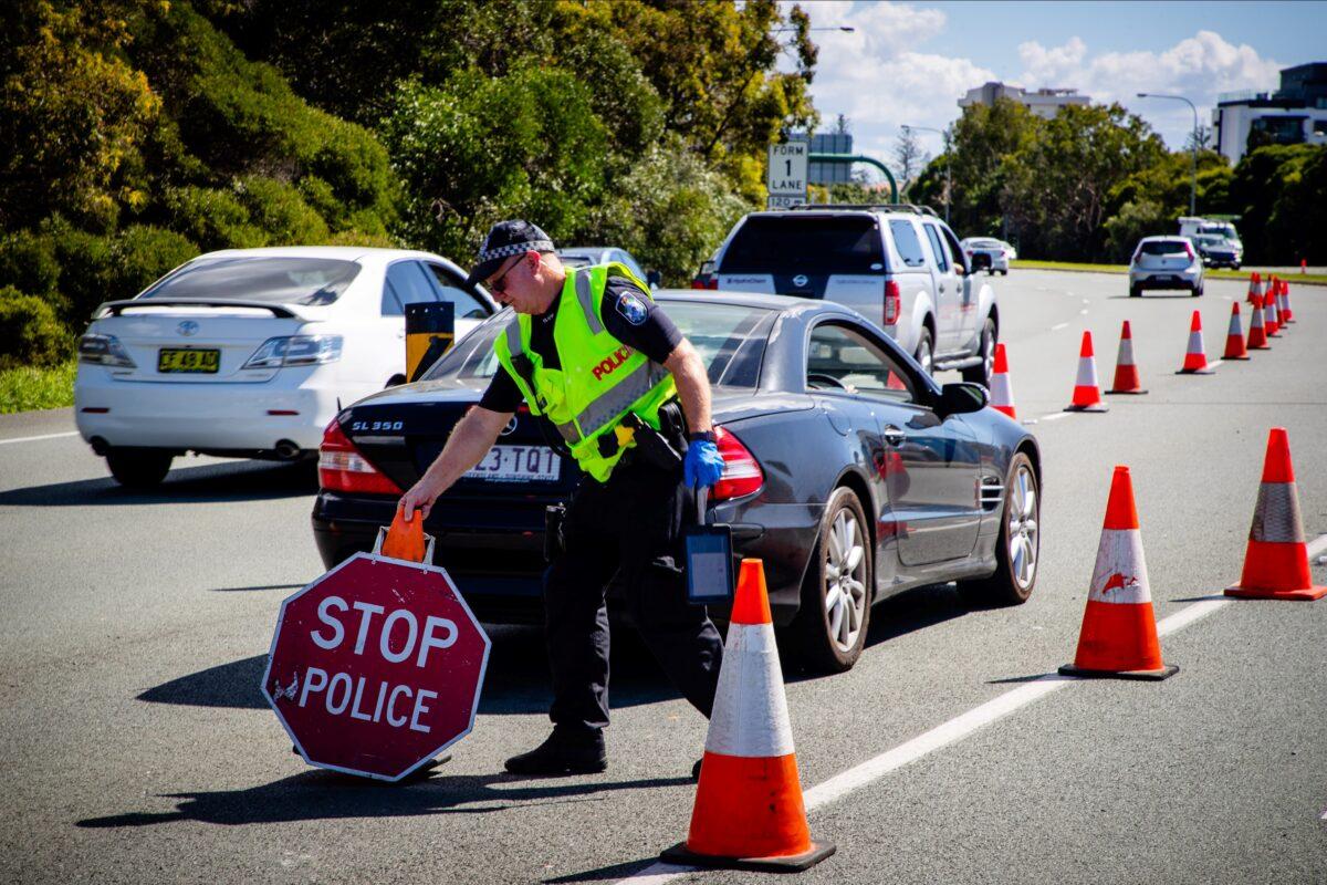 A Queensland police officer moves a stop sign at a vehicle checkpoint on the Pacific Highway on the Queensland—New South Wales border, in Brisbane on April 15, 2020. (Patrick Hamilton/AFP via Getty Images)
