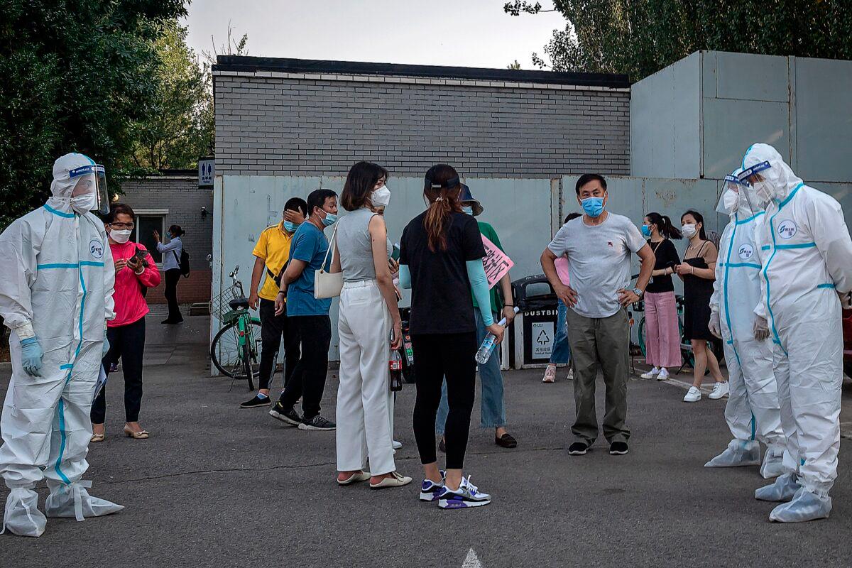 Workers wearing personal protective equipment (PPE) take care of a group of people wearing face masks as they wait to undergo COVID-19 coronavirus tests in Beijing, China, on June 19, 2020. (Nicolas Asfouri/AFP via Getty Images)