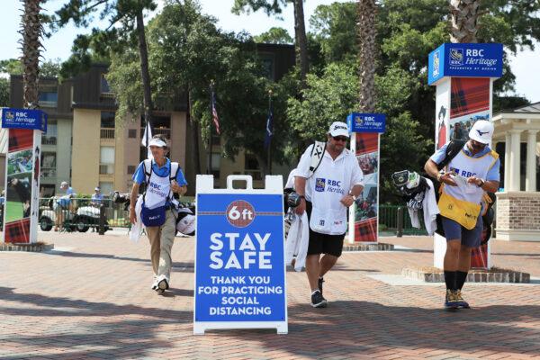Caddies walk past signage promoting social distancing as a COVID-19 precaution during the second round of the RBC Heritage at Harbour Town Golf Links in Hilton Head Island, S.C., on June 19, 2020. (Streeter Lecka/Getty Images)