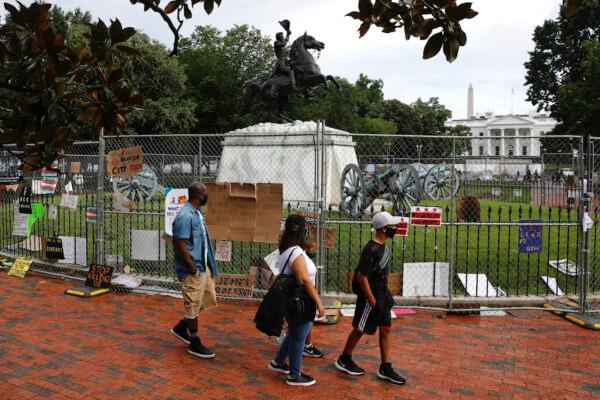 People walk past protest signs affixed to fencing surrounding a statue of President Andrew Jackson in Lafayette Park near the White House on June 20, 2020. (AP Photo/Patrick Semansky)