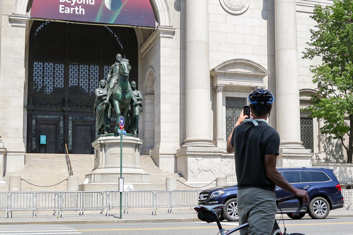 A cyclist takes photos of the Theodore Roosevelt Statue in front of the American Museum of Natural History in New York on June 23, 2020. (Chung I Ho/The Epoch Times)