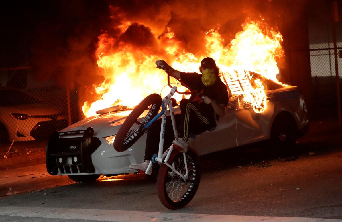 A man on a bicycle rides past a burning police car during a demonstration next to the city of Miami Police Department in Miami, Fla., on May 30, 2020. (Wilfredo Lee/AP Photo)
