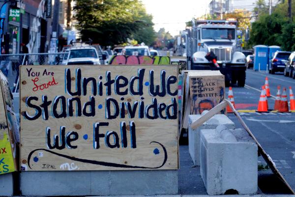 A sign on a barricade reads "united we stand divided we fall," as a truck and other heavy equipment from the Seattle Department of Transportation is staged at the the CHOP (Capitol Hill Occupied Protest) zone in Seattle, Wash., on June 26, 2020. (Ted S. Warren/AP Photo)