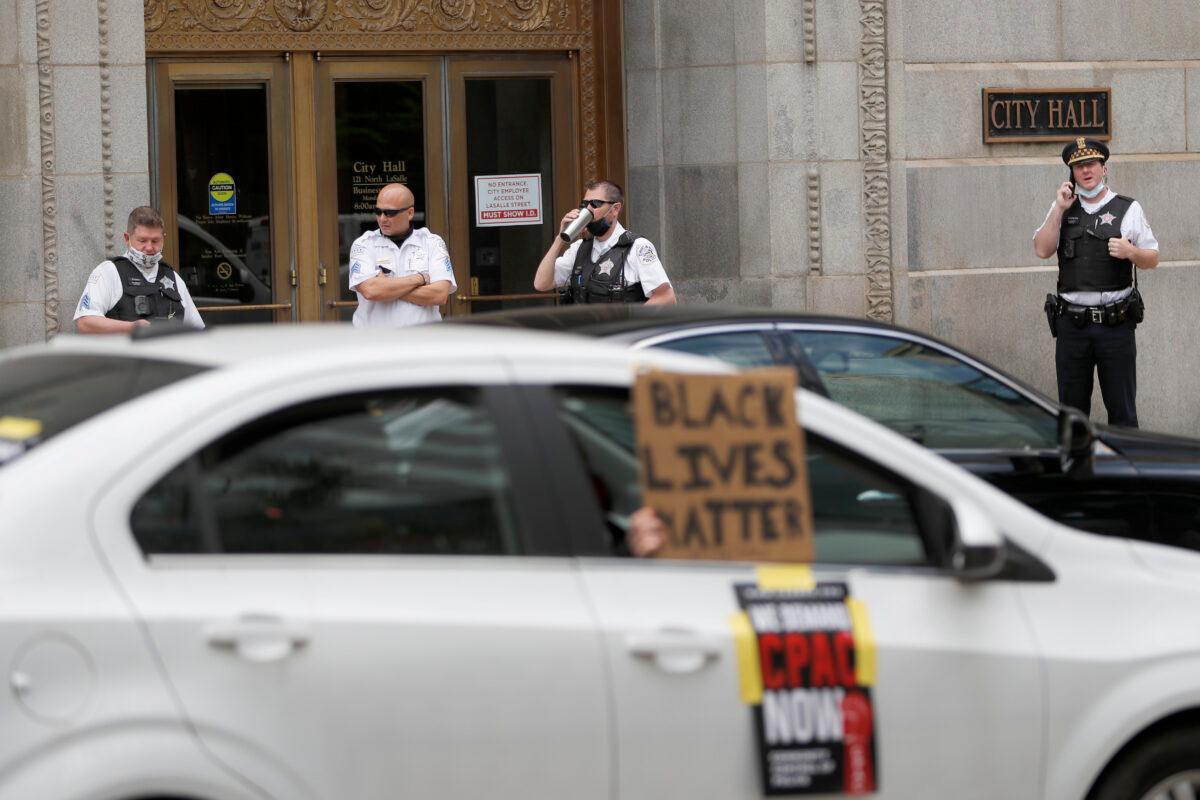 Chicago police officers stand outside City Hall, watching as a caravan of protesters demand that Mayor Lori Lightfoot enact the ordinance for an all-elected Civilian Police Accountability Council, CPAC, on June 17, 2020. (Charles Rex Arbogast/AP Photo)