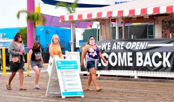 People wearing facemasks walk past a health and safety guideline board and an open restaurant on Santa Monica Pier which re-opened on June 25 after closure for over three months due to the coronavirus pandemic in Santa Monica, California, on June 26, 2020. (Frederic J. Brown/AFP via Getty Images)