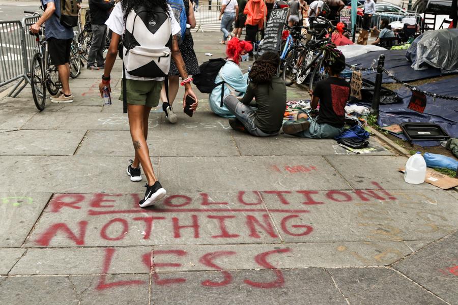“Revolution Nothing Less” is painted onto the sidewalk as activists and protesters occupy an area across from City Hall in Manhattan before a City Council decision on police funding in New York on June 30, 2020. (Charlotte Cuthbertson/The Epoch Times)